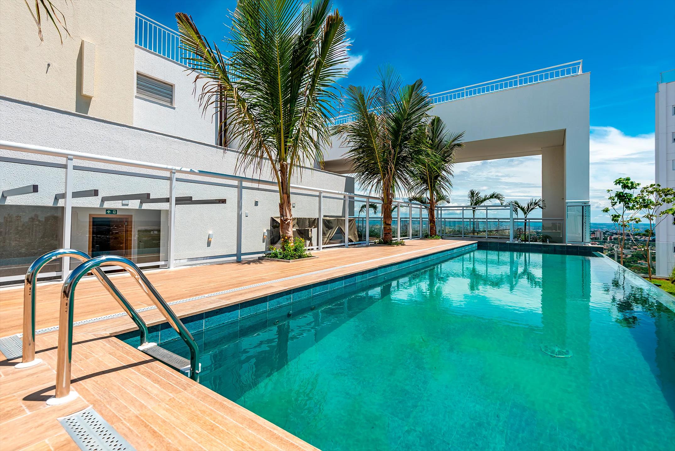 Piscina do rooftop com palmeiras e deck de madeira sob céu azul