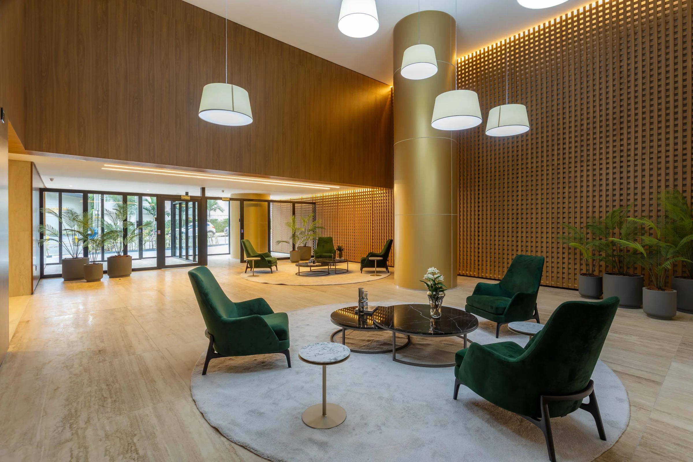Lobby com poltronas verdes, pendentes e painéis de madeira