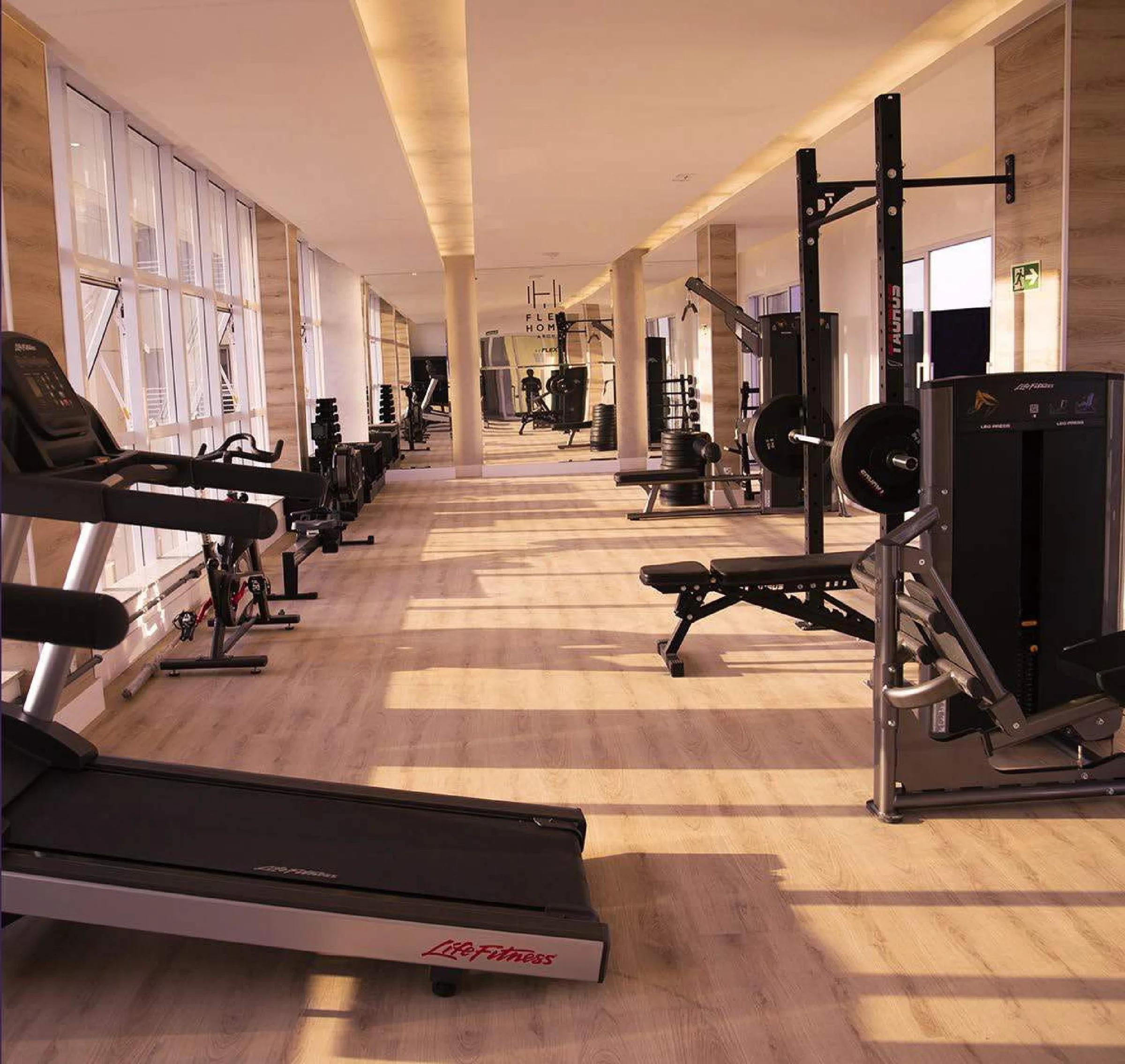 Academia equipada com esteiras, banco de musculação e aparelhos com iluminação natural