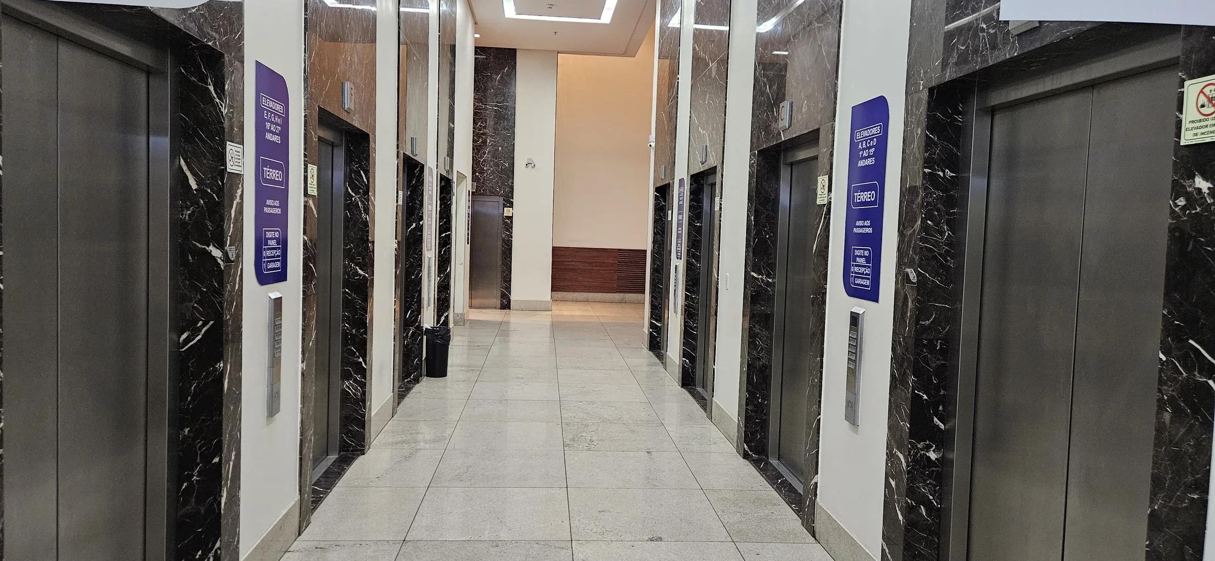 Hall de elevadores com painéis em mármore escuro e iluminação embutida no teto
