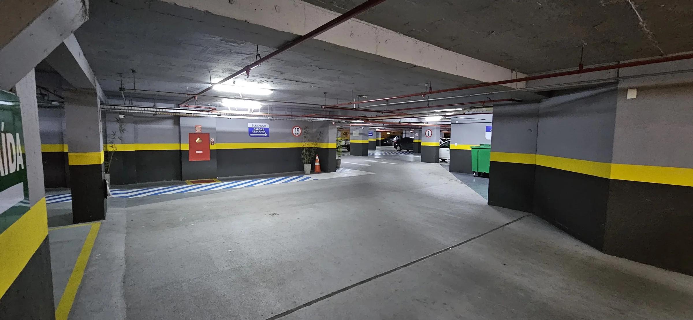 Estacionamento coberto com vagas demarcadas e sinalização nas paredes e pilares