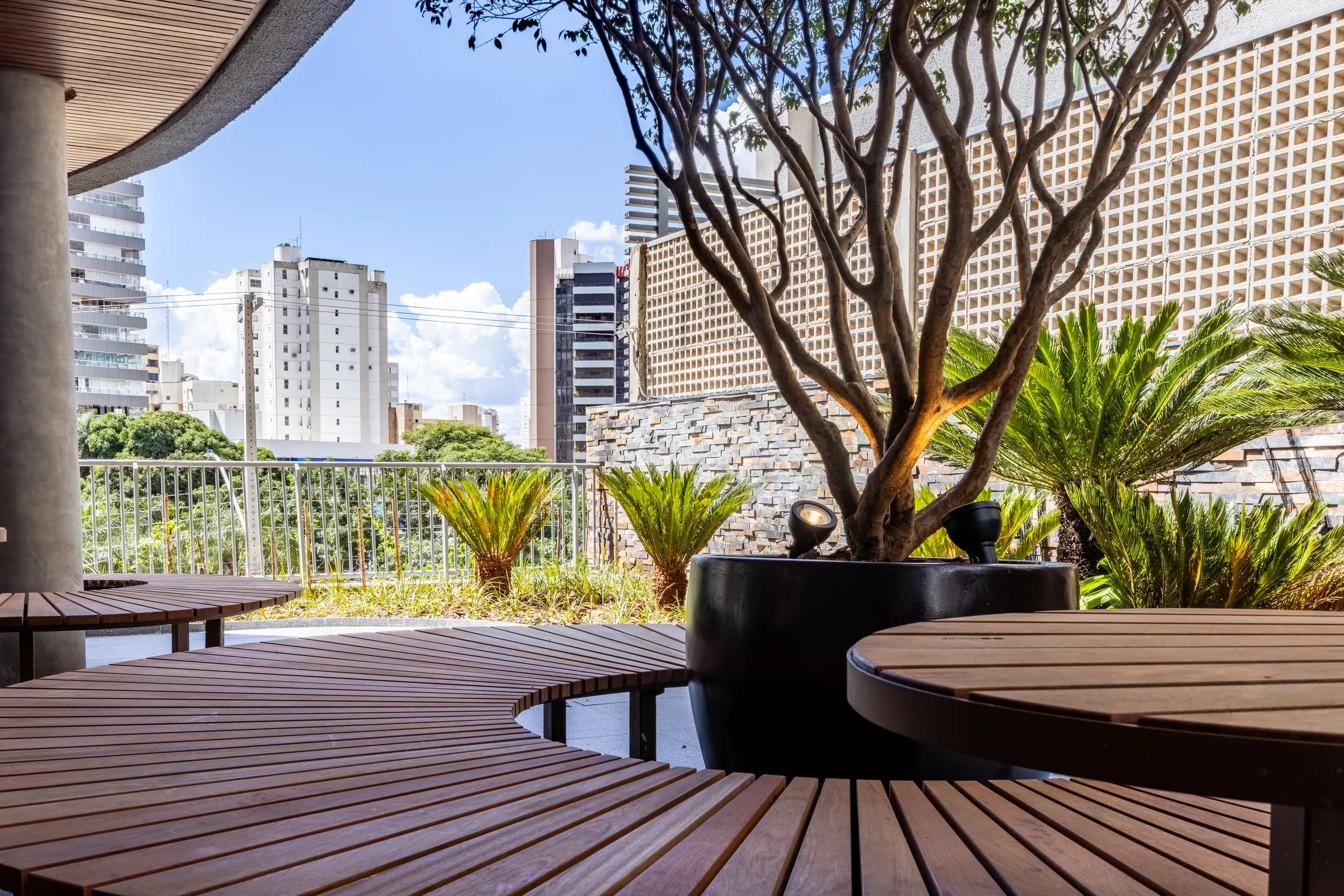 Perspectiva de lounge externo com bancos, jardineiras e árvores.