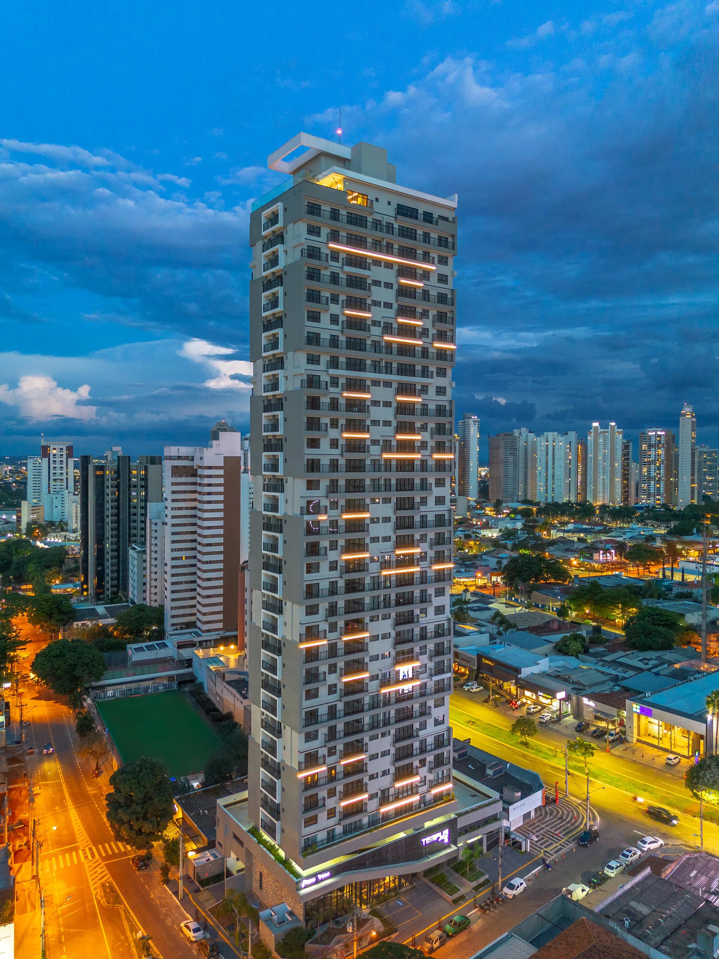 Fachada do edifício residencial iluminada ao anoitecer com vista aérea urbana