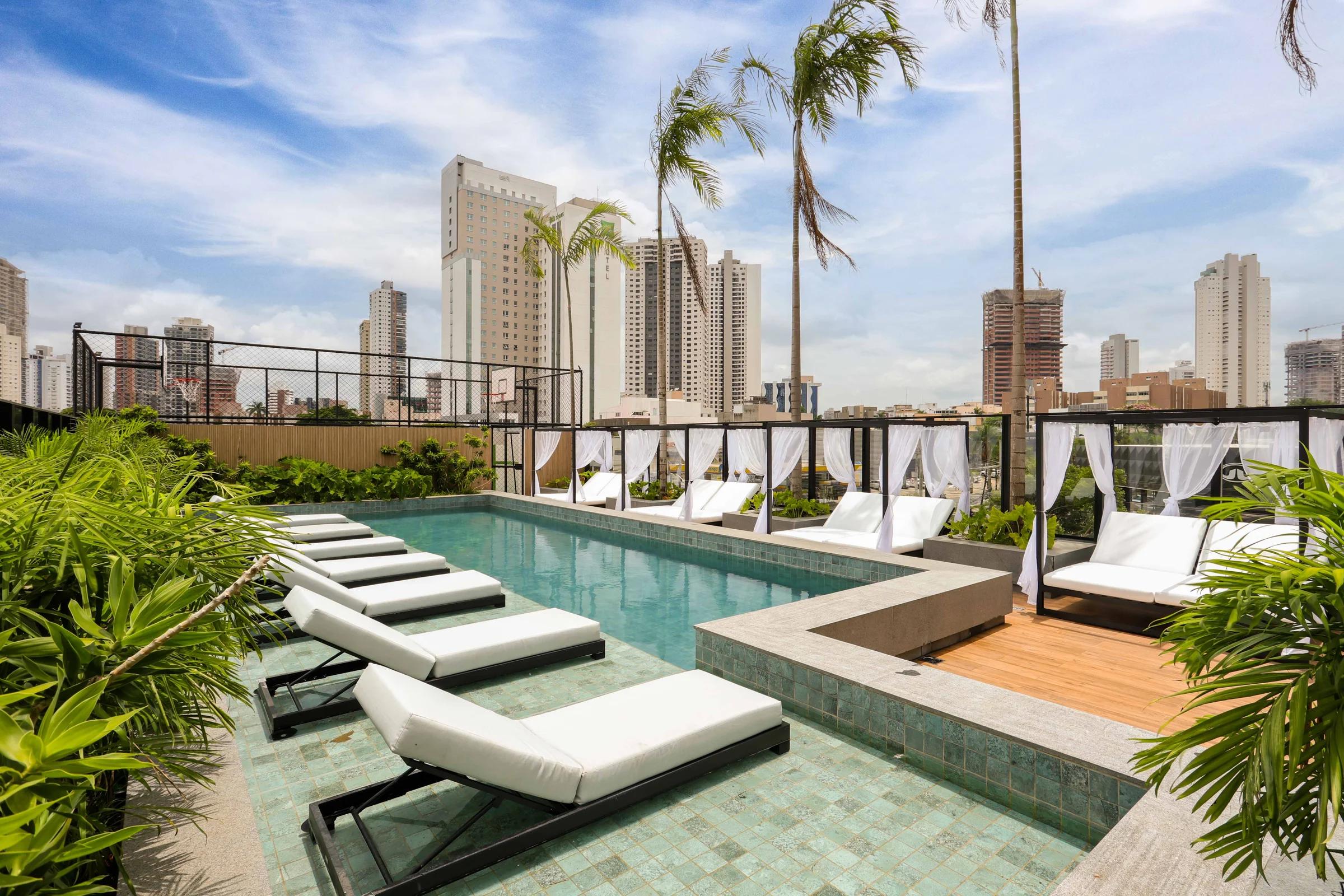 Piscina do rooftop com espreguiçadeiras, cabanas e vista da cidade
