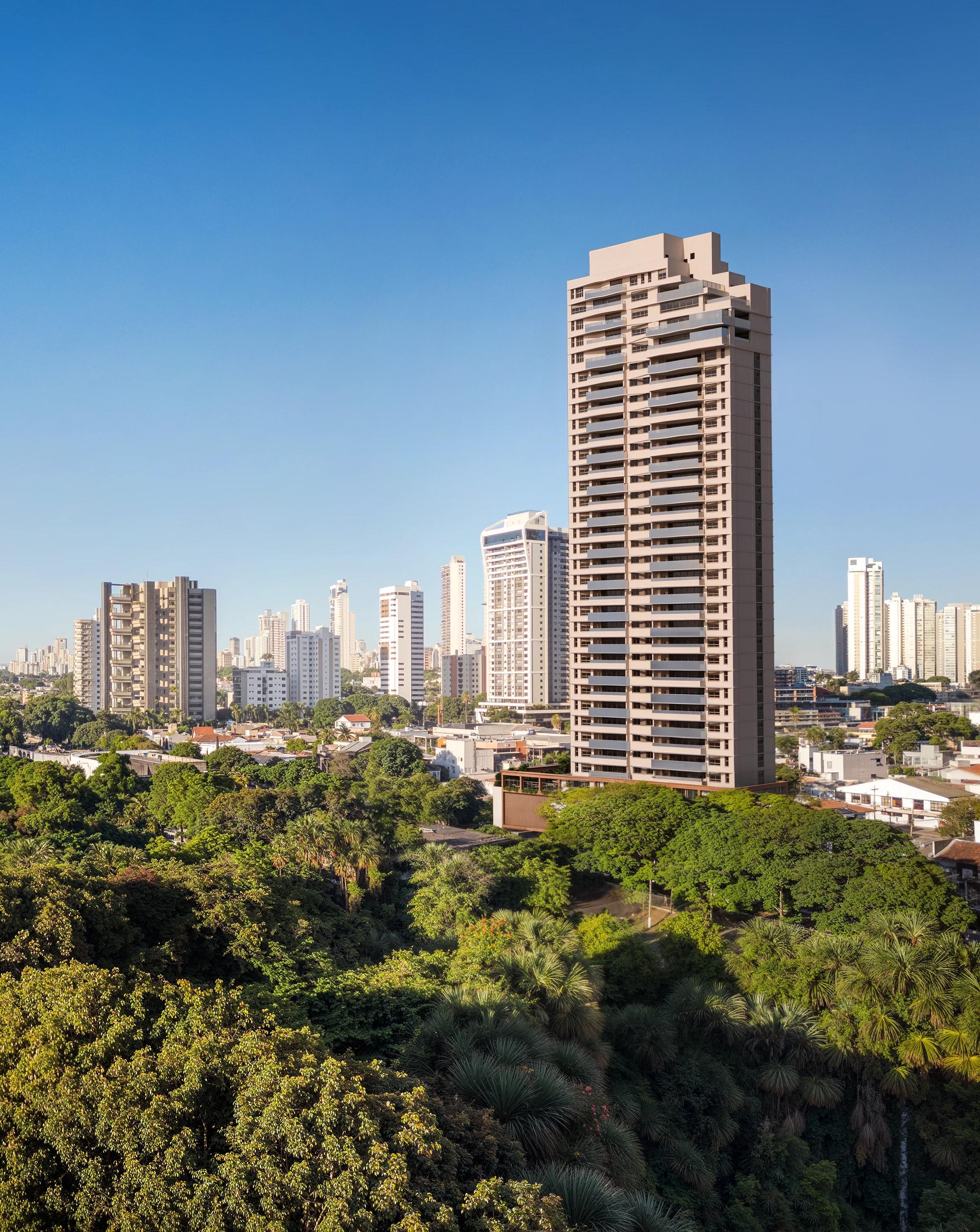 Perspectiva da fachada inteira do edifício inserida no skyline urbano cercado por área verde